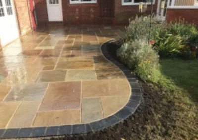 Curved patio with natural stone paving and dark brick edging