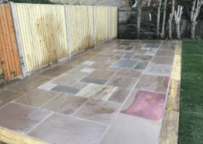 Freshly laid sandstone patio beside wooden garden fence