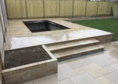 Modern garden patio with raised pond, tiled steps, and beige paving