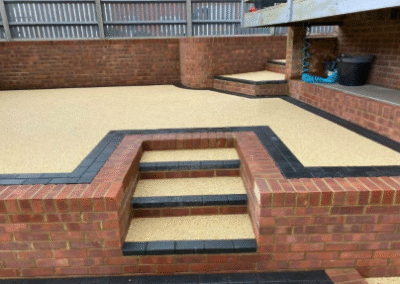 Resin patio with brick retaining walls and black-edged steps in garden